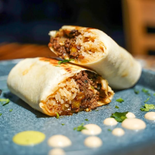 Two halves of a burrito filled with seasoned meat and rice, garnished with sauces and herbs.