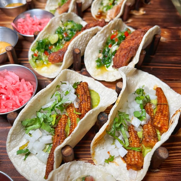 Close-up of several tacos with various fillings, including baby corn, on a wooden serving board.