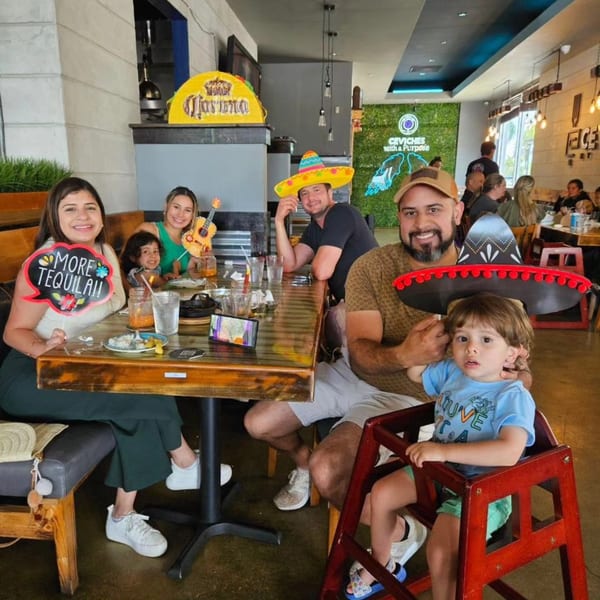 A family with children, wearing sombreros, smiling at a table in A Taco by Divino restaurant.