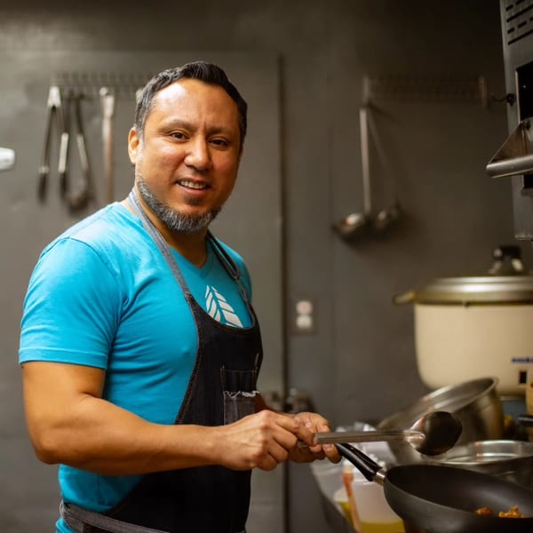 A smiling chef in a blue shirt and apron cooks in a pan at A Taco by Divino.