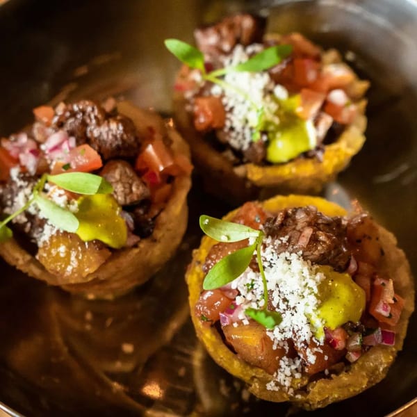 Three mini tacos with meat, pico de gallo, cheese, and green sauce, garnished with microgreens.