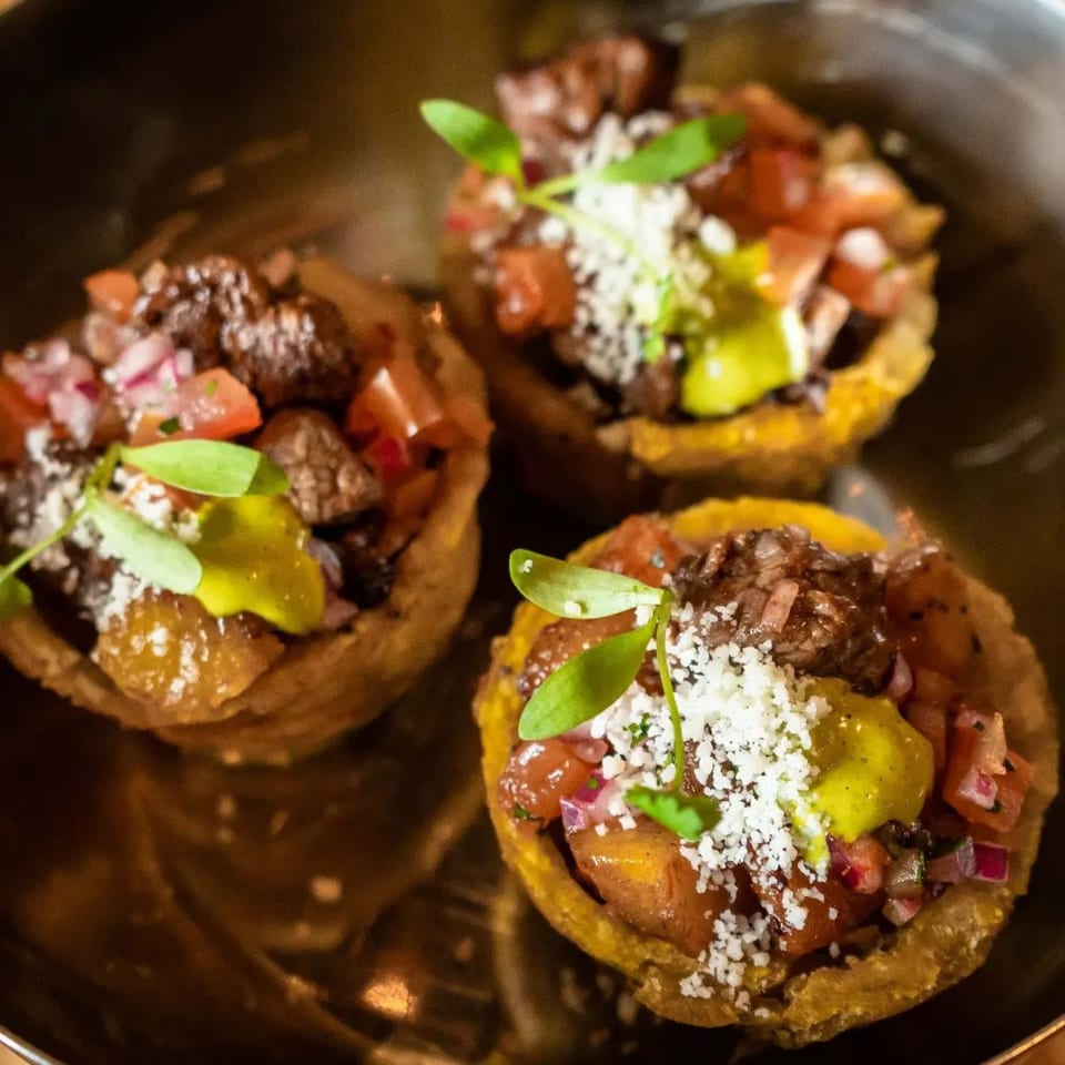 Three mini tacos with meat, pico de gallo, cheese, and green sauce, garnished with microgreens.