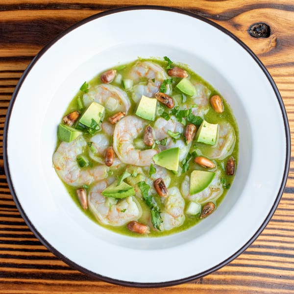 Shrimp ceviche with avocado, cilantro, and corn nuts in a vibrant green sauce.