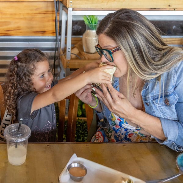 A young girl helps a woman take a bite of a taco at A Taco by Divino.